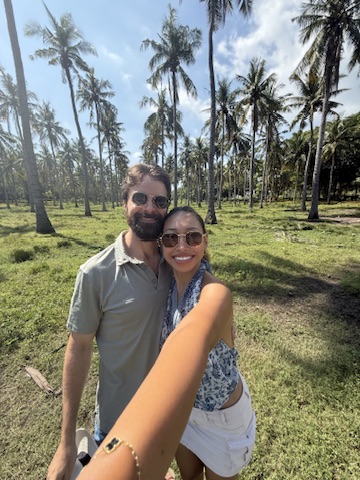 Michael and Deha smiling together in a tropical grove